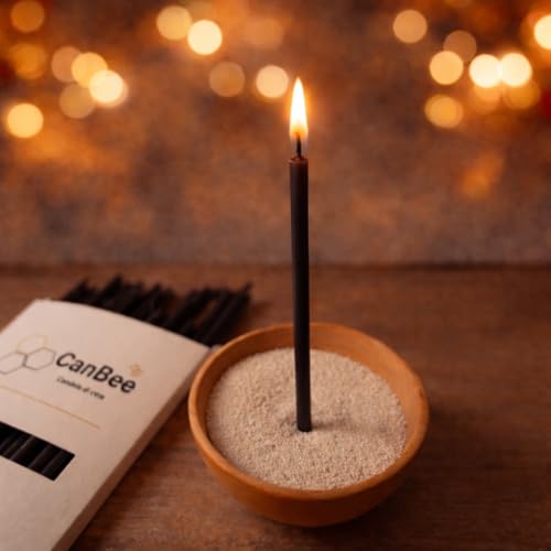 Candela sottile nera accesa in una ciotola di sabbia accanto a una confezione CanBee, con luci sfocate sullo sfondo
