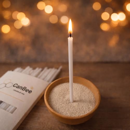 Candela sottile bianca accesa in una ciotola di sabbia accanto a una confezione CanBee, con luci sfocate sullo sfondo